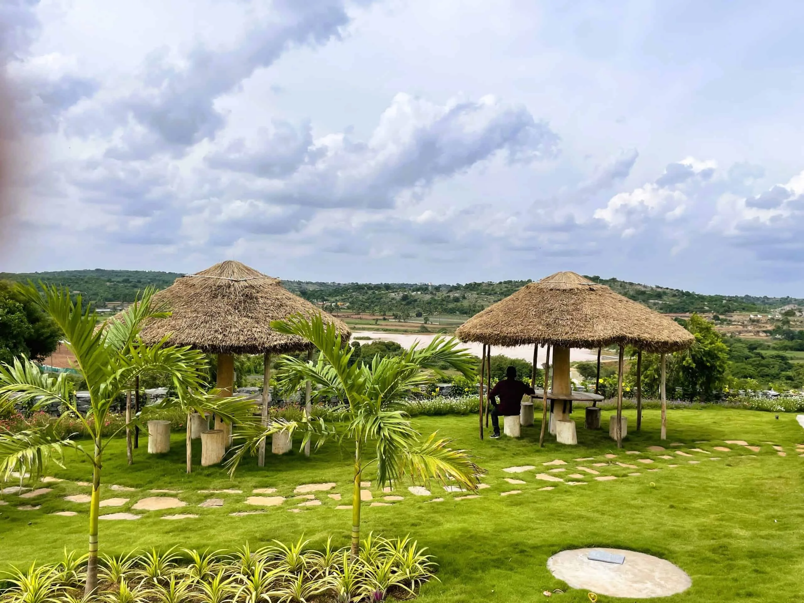 Thatched sit-outs on a green lawn at Ecoland Farms, looking out over the valley